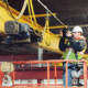 CraneWerks employee in a black hoodie, hi-vis safety green safety vest, and white hard hat performing a hoist inspection in an orange lift