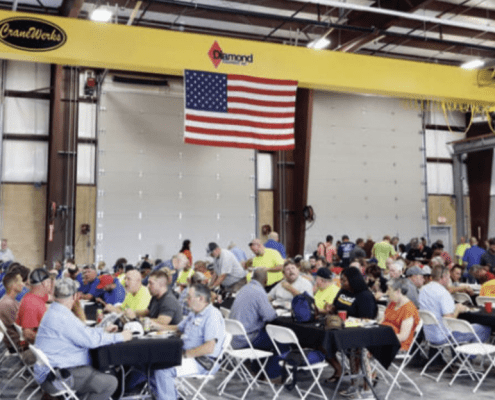 Lunch being served to a large group of people sitting under an American flag and CraneWerks overhead bridge crane at the new Diamond Equipment location.