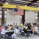 Lunch being served to a large group of people sitting under an American flag and CraneWerks overhead bridge crane at the new Diamond Equipment location.